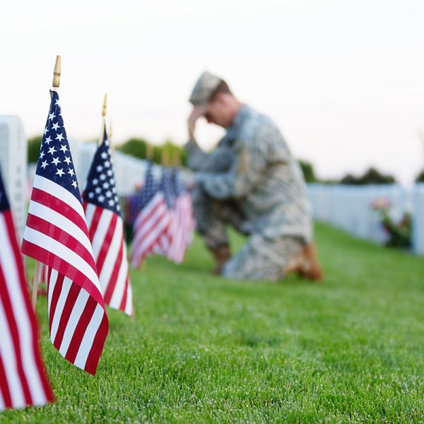 American soldier kneeling at a veterans grave on memorial day. Focus on the foreground.