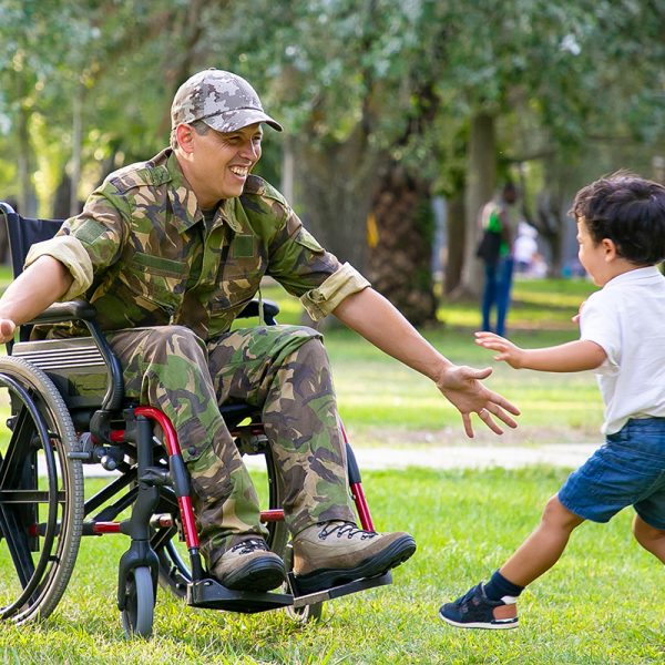 Cheerful kids meeting military dad and running to disabled man in camouflage with open arms for hug. Veteran of war or returning home concept